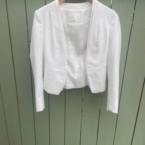 Vit kavaj från H&M,st.34 - Snygg vit kavaj från H&M med öppen front och figurnära passform. Jackan har långa ärmar och två fickor framtill. Perfekt för en stilren look och enkel att matcha med olika outfits.Jätte fin elegant kavaj i storlek 34 kan även passa 36 tror jag. Tror den är oanvänd helt ny. Hämtas i norsborg botkyrka eller fraktas så fort så möjligt pågrund av flytt. Skynda fynda. Säljer allt hemma se mina andra saker jag säljer