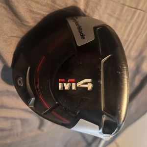 TaylorMade M4 Driver - Säljer en TaylorMade M4 driver med svart och silver klubbhuvud och röd detalj. Klubbhuvudet är stort och aerodynamiskt, skaftet är silverfärgat. Perfekt för golfare som vill ha extra längd och förlåtande egenskaper på utslagen.