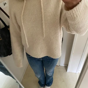 Beige stickad hoodie - Mysig beige stickad hoodie med huva. Tröjan har lång ärm och en avslappnad passform.