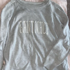 Ljusgrå stickad tröja från GANT - Säljer en ljusgrå stickad tröja från GANT med broderad text framtill. Tröjan har rund halsringning och långa ärmar. 