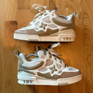 Louis Vuitton Skate Sneakers - Snygga Louis Vuitton sneakers i beige och vitt med LV-logga och blommig detalj på sidan. Skorna har chunky sula, meshpaneler och skinnpartier samt grova snören. De är i storlek 41. Skorna är använda men är fortfarande i bra skick. Box och dustbags följer med. Perfekta för dig som gillar exklusiva och trendiga sneakers med streetkänsla. Pris kan diskuteras