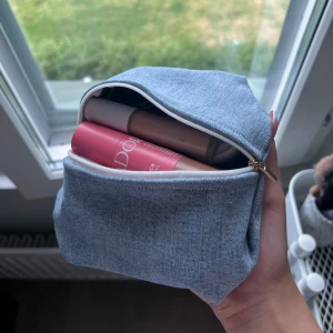 Mini necessär med dragkedja - Säljer en stilren och praktisk necessär i ljusblått jeanstyg. Väskan har en enkel, boxig form och stängs med vit dragkedja. Perfekt för smink eller småprylar och lätt att ta med i väskan. Snygg och enkel design som passar till allt.