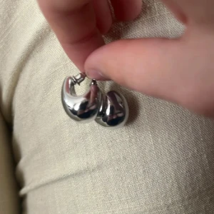 Chunky droppformade örhängen i silver - Säljer ett par chunky örhängen i droppform med blank, silvrig finish. De har en modern och cool vibe, perfekta för att lyfta din stil. Örhängena är i metall och har en unik, rundad design som verkligen syns.