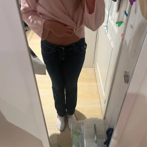 Mörkblå bootcut jeans med kontrastsömmar - Säljer ett par mörkblå jeans med bootcut-modell och tydliga vita kontrastsömmar. Byxorna har låg midja, klassiska fickor fram och bak med snygga detaljer och knappstängning. Stolek 158