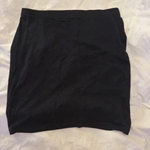 Svart enkel kortkjol - En basic svart kortkjol med rak passform. Kjolen är stilren och lätt att matcha till olika outfits. Perfekt för dig som gillar minimalistisk stil och vill ha en enkel kjol i garderoben.