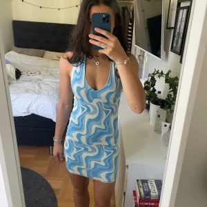 Blå och vit mönstrad klänning Gina Tricot - Säljer en kort, tight klänning från Gina Tricot i storlek XS. Klänningen har ett vågigt blått och vitt mönster, v-ringning och är ärmlös med öppen rygg.