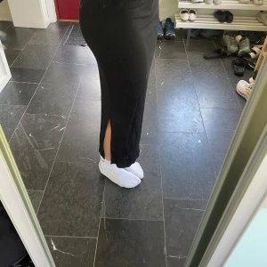 Svart ribbad långkjol från 157 XS - Svart långkjol från 157 i ribbad stretchig bomull. Kjolen har en slim passform och en snygg slits på sidan som ger extra edge. Jätteskönt material! 