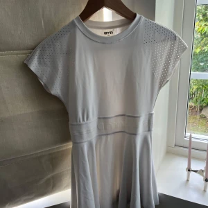 Vit tennisklänning från Aimn - Supersnygg vit tennisklänning från Aimn med perforerade detaljer på axlarna och ett markerat midjeband med broderad logga. Klänningen har rund hals och korta ärmar, tillverkad i mjukt och stretchigt syntetmaterial som ger en sportig vibe. Den har inte inbyggda shorts.