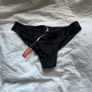 Svarta bikiniunderdelar från Nelly - Svarta bikiniunderdelar från NLY Beach med snygg scrunch-detalj bak för en extra flattering fit. Modellen är klassisk med låg skärning och mjukt, stretchigt syntetmaterial som sitter bekvämt. Perfekt för strandhäng och poolparty i sommar! Helt nya och oanvända!