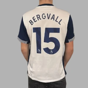 Bergvall tröja  - Säljer en vit och blå fotbollströja från Nike med Tottenham Hotspur-logga och AIA sponsortryck. (BERGVALL) Tröjan har korta ärmar med Premier League-märke och texten 'No room for racism'. Perfekt för fans av Spurs! Helt oanvänd