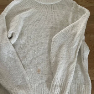 Vit stickad tröja från 157 - Mysig vit stickad tröja från 157 med ribbad krage och långa ärmar. Enkel och klassisk design som passar perfekt till lager-på-lager. Tröjan är i en ljus nyans och har en skön, lite loose passform. Har några fläckar som man ser på bilderna, kanske går bort om man försöker 