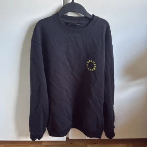 Svart sweatshirt Axel Arigato med tryck - Svart sweatshirt från Axel Arigato med coolt gult tryck i japanska tecken både fram och bak. Tröjan har rund hals, ribbade muddar och är långärmad. Perfekt för dig som gillar streetwear och vill sticka ut med en unik design.