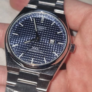Tissot PRX Powermatic 80 blå stål - Snygg Tissot PRX Powermatic 80 med blå urtavla och coolt rutmönster. Klockan har ett stilrent armband i rostfritt stål och datumvisning vid klockan tre. Klassisk design med silverfärgade detaljer och markerade index. Perfekt accessoar för dig som gillar stilren look.