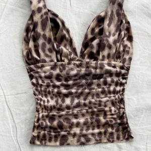 Leopardmönstrad croppad topp - Snygg croppad topp med leopardmönster i beige och bruna toner. Djup v-ringning och breda axelband ger en trendig look. Perfekt att styla med jeans eller kjol för en cool outfit.