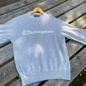 Grå Champion sweatshirt med broderad logga - Säljer en grå sweatshirt från Champion i storlek S. Tröjan har ett broderat Champion-tryck i vitt över bröstet, rund hals och långa ärmar. Hör av dig vid frågor!