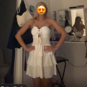 Vit kort klänning med snörning - Supersöt vit kort klänning med volanger och snörning framtill. Axelbandslös design som ger en fräsch och somrig vibe. Perfekt för dig som vill ha en romantisk och lätt look. Materialet känns luftigt och bekvämt, och klänningen har en feminin passform.