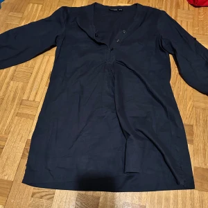 Mörkblå henley-skjorta från Esmara - Mörkblå henley-skjorta från Esmara med v-ringning och tre knappar framtill. Skjortan har lång ärm och är tillverkad i mjuk bomull, perfekt för en avslappnad och stilren look.