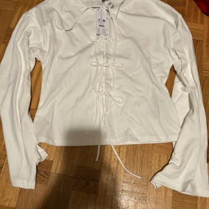 Vit långärmad topp med snörning Gina Tricot - Säljer en fräsch vit långärmad topp från Gina Tricot i storlek L. Toppen har snygg snörning framtill med flera knyt och är tillverkad i mjuk bomullsmix. Perfekt för dig som gillar stilrena och trendiga detaljer.