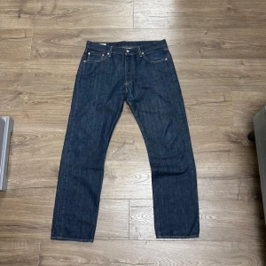 Levi's 501 - Klassiska Levi's 501 jeans i mörkblå denim med raka ben och normal passform. Byxorna har fem fickor, gul kontrastsöm och ikonisk läderpatch bak i midjan. Perfekta för dig som gillar tidlös stil och schysst kvalitet.