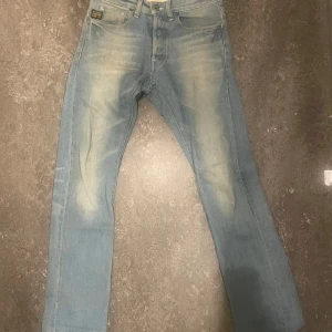Ljusblå jeans från G-Star RAW - Säljer ett par ljusblå jeans från G-Star RAW med klassisk femficksdesign och snygga slitningar framtill. Jeansen har raka ben och coola detaljer som G-Star-logga på bakfickan och vid myntfickan. Perfekta för dig som gillar en avslappnad streetstil.