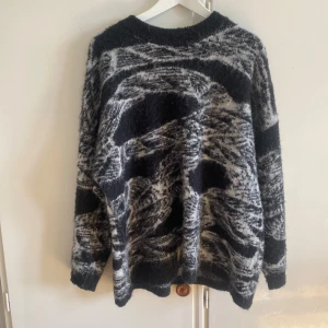 Svartvit stickad tröja missäy  - Mysig stickad tröja från Gidéon & Co Paris i svart och grått med abstrakt mönster. Tröjan har lång ärm, rund hals och en lite fluffig känsla. Perfekt för dig som gillar en chill och unik look under kyliga dagar.