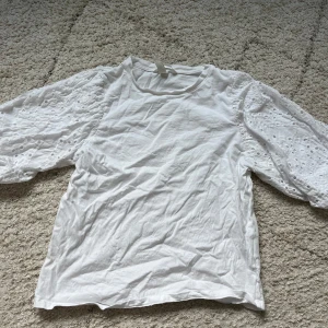 Vit blus med broderade ärmar - Supersöt vit blus från H&M i storlek XS. Toppen har puffiga, broderade trekvartsärmar med hålmönster och rund halsringning. Perfekt för dig som gillar romantiska detaljer och en fräsch look.