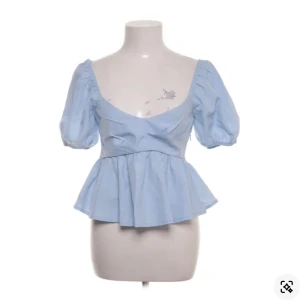 Ljusblå volangblus från NA-KD - Supersöt ljusblå blus från NA-KD med puffiga korta ärmar, djup v-ringning och volang nertill. Toppen har en feminin siluett och är gjord i mjuk bomull, perfekt för vår och sommar. Enkel att styla med både jeans och kjol. Köpt via Sellpy, lappen kvar!