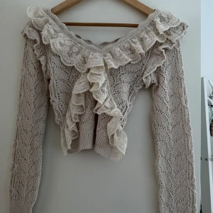 Beige stickad tröja med spetsvolang från Zara - Superfin beige stickad tröja från Zara med bred spetsvolang runt halsen och framtill. Typ oanvänd. Den är croppad