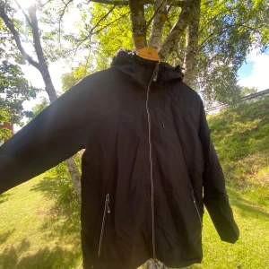 Svart vindjacka med huva och dragkedja - Svart vindjacka med huva och hel dragkedja framtill. Från C stuf.