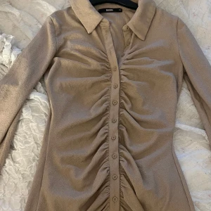 Beige kortklänning från Bik Bok XS - Supersnygg beige kortklänning från Bik Bok i storlek XS. Klänningen har långa ärmar, krage och knappar hela vägen framtill. 