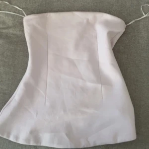 Ljusrosa bandeau tubtopp - Säljer en ljusrosa bandeau tubtopp med enkel och stilren design. Toppen är axelbandslös och har en lätt utsvängd form nertill. Perfekt för varma dagar eller som layering-piece.