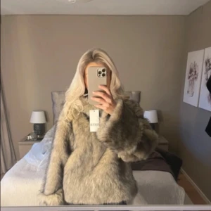 Beige pullover pälsjacka med oversized passform - Säljer en fluffig beige pullover pälsjacka med breda ärmar och hög krage. Jackan har en oversized look och är perfekt för dig som vill sticka ut med en mysig och trendig vibe. Passar till både jeans och kjol för en cool stil.