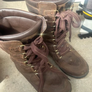 Bruna mockakängor med snörning - Rejäla bruna kängor i mocka med snörning och guldfärgade öljetter. Insidan är fodrad med mjukt material för extra värme. Perfekta för kyligare dagar och har en klassisk outdoor-look.