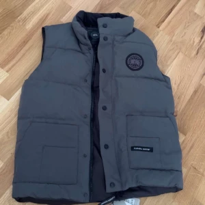 Obs. Mötas upp Stockholm Grå dunväst från Canada Goose -  S men funkar M också. Säljer en grå dunväst från Canada Goose med hög krage, två stora fickor framtill och klassisk logotyp på bröstet. Västen har både dragkedja och knappar framtill för extra skydd mot kylan. 