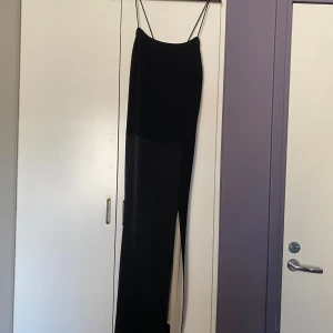 Svart Filippa K långklänning med tunna axelband  - Säljer en svart långklänning med tunna axelband och snygg layering-effekt från Filippa K. Klänningen har en rak siluett och är fodrad med champagnefärgad polyester. Perfekt för dig som gillar minimalistisk stil och vill ha något elegant med en twist. Använd 1gång.