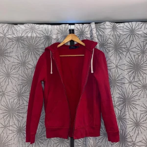 Röd hoodie från Polo Ralph Lauren - Säljer en röd hoodie från Polo Ralph Lauren med dragkedja och vit snörning i huvan. Tröjan har långa ärmar, två stora fickor fram och en liten blå Polo-logga på bröstet. Perfekt för chill dagar och snygg streetstyle.
