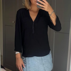 Svart blus med glitterdetaljer  - Snygg svart blus med v-ringning och glitter sömmar längs halsen och ärmsluten. Den perfekta stilrena blusen med det lilla extra. 