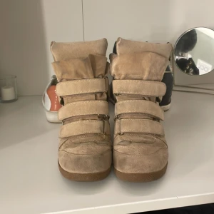 Isabell marant - Snygga beige sneakers med inbyggd kilklack och flera breda kardborreband. Skorna har en cool, sportig design och är gjorda i mocka för en mjuk känsla. Perfekta för dig som vill ha lite extra höjd men ändå en avslappnad look.