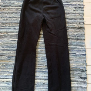 Svarta mjukisbyxor med snörning - Svarta mjukisbyxor med raka ben, elastisk midja och snörning framtill. Byxorna har två stora fickor framtill och är gjorda i mjukt bomullsmaterial. Perfekta för chill dagar eller när du vill vara bekväm men ändå se stilren ut.