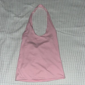 Rosa halterneck linne Gina Tricot XS - Supersött ljusrosa halterneck-linne från Gina Tricot i mjuk bomull. Linnet har en djup urringning och är ärmlöst, perfekt för varma dagar eller när du vill ha en chill och trendig look. Enkel och stilren design som är lätt att matcha med jeans eller kjol.