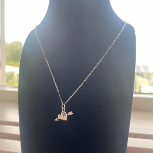 Silverhalsband med hjärta och pil - Sött halsband i silverfärg med ett hängsmycke format som ett hjärta genomborrat av en pil. Kedjan är tunn och smidig, perfekt för att ge en romantisk touch till din stil. Passar dig som gillar enkla men ändå personliga smycken. Rostfri kjedjan är 40cm lång 💘