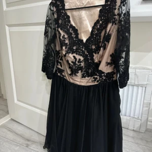 Svart spetsklänning med champagnefärgad botten - Snygg långklänning med champagnefärgad botten och svart spetsdetaljer. Klänningen har omlott-v-ringad överdel, halvtransparenta spetsärmar och ett flowigt svart kjolparti. Perfekt för dig som vill sticka ut med eleganta detaljer och cool kontrast. Använd 1 gång, några timmar 