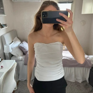 Draperad bandeau topp - Draperad bandeau topp med två ståltrådar fram som på en korsett, så att den hålls upp. Det står ingen storlek men skulle säga mellan S-M. Den har en dragkedja längs bak så den är lätt att sätta på. Skriv om du har fler frågor!☺️