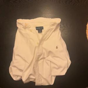 Vit skjorta från Ralph Lauren - Klassisk vit skjorta från Ralph Lauren med broderad logga på bröstet. Skjortan står i storlek xl (18-20) men motsvarar folk som har S och m jätte bra. Perfekt för dig som gillar stilrena och exklusiva kläder. Nypris 1600 mitt pris 500, pris kan självklart diskuteras!!