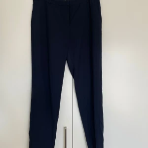 Mörkblå kostymbyxor från Mango - Snygga mörkblå kostymbyxor från Mango med klassisk rak passform och hällor för bälte. Perfekta till en dressad look och tillverkade i ett mjukt material som känns bekvämt hela dagen.