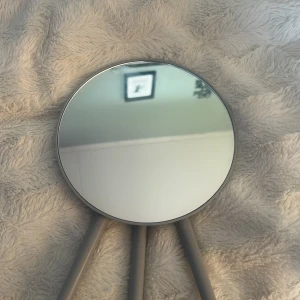 Rund sminkspegel med grå stativ - Snygg rund sminkspegel med tre grå ben i matt plast. Spegeln har en minimalistisk design och är perfekt att ställa på sminkbordet eller ta med till resan. Diameter ca 20 cm. Enkel att fälla ihop och flytta runt. Passar dig som vill ha en stilren look på rummet.