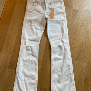 Chunky low flare jeans creme 164 - Chunky low flare jeans i cremefärg med slitna detaljer på benen. Byxorna har låg midja, klassiska fem fickor och vida ben med flare. 