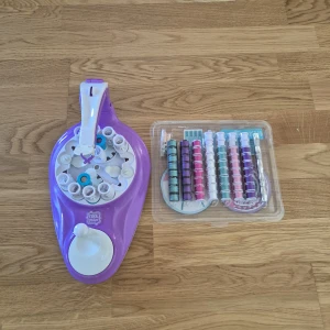 Cool Maker armbandsmaskin med trådar - Cool Maker armbandsmaskin i lila och vitt, perfekt för att skapa egna armband. Medföljer flera färgglada trådrullar i rosa, blått, lila och silver för att designa unika smycken. Enkel att använda och superkul för dig som gillar DIY.