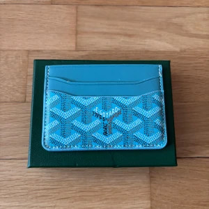 Goy4rd Plånbok - Säljer en snygg blå plånbok med deras ikoniska mönster. Plånboken har flera kortfack och är tillverkad i skinn med ett stilrent tryck. Perfekt för dig som vill ha något unikt och trendigt i fickan.