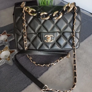 Svart quiltad C-axelväska - Säljer en ikonisk svart axelväsk ii quiltat skinn med guldfärgade kedjedetaljer och klassiskt CC-spänne framtill. Väskan har en elegant och tidlös design som lyfter vilken outfit som helst.